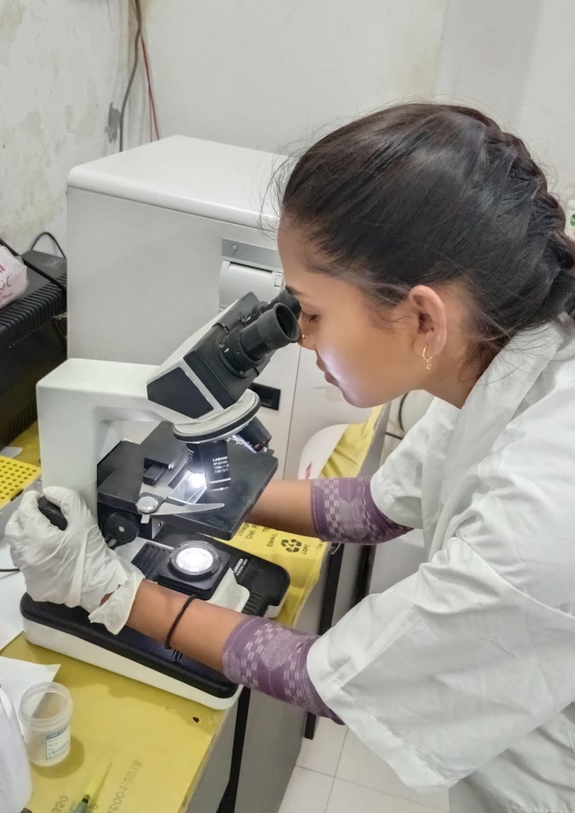Ms. Priyanka Desai examining a slide under the microscope — Sun Pathology Laboratory, Waghodia